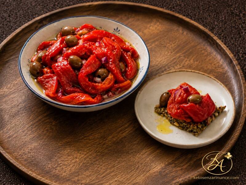 Peperoni arrostiti con olive taggiasche e cipolla di Tropea, serviti in una ciotola mediterranea e accompagnati da un cracker chetogenico con peperoni sfilacciati. Una preparazione semplice, saporita e versatile, perfetta come antipasto, contorno oppure b
