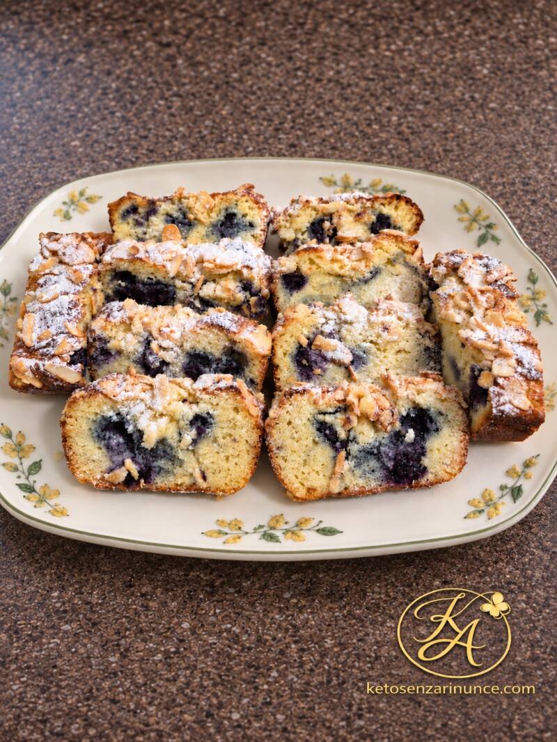 Fette di plumcake chetogenico al mascarpone e mirtilli, dalla mollica morbida e dalla copertura croccante, disposte su un vassoio floreale.