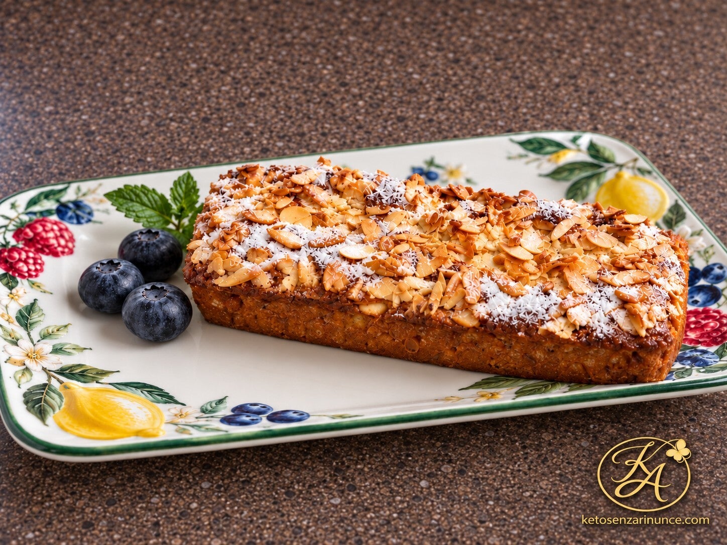 Plumcake chetogenico al mascarpone e mirtilli con copertura dorata e croccante di mandorle a lamelle, servito su un vassoio decorato con limoni e frutti di bosco