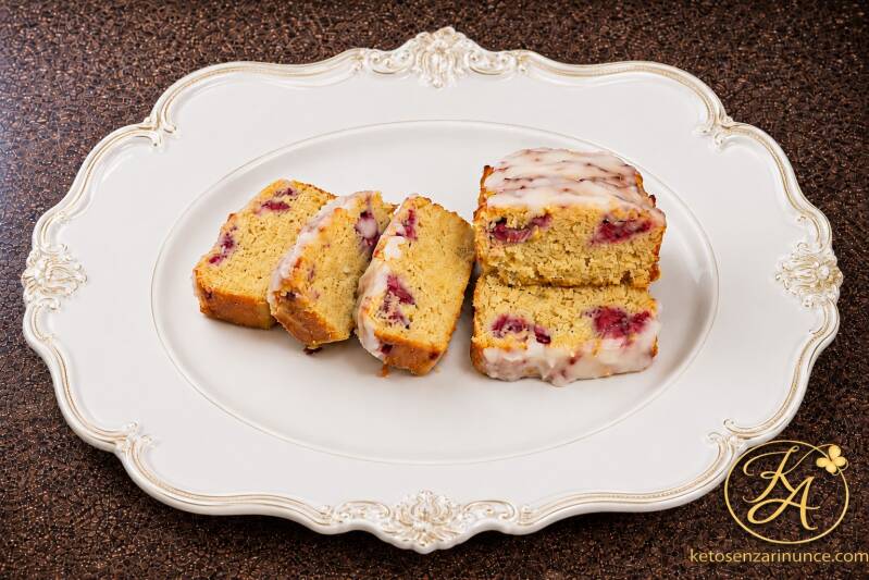 Plumcake keto alla panna e lamponi, morbido e profumatissimo, servito su piatto bianco elegante con velo di glassa e noci tritate. Ricetta chetogenica dolce per colazione o merenda, preparata nella cucina di Oxi per ketosenzarinunce.com.