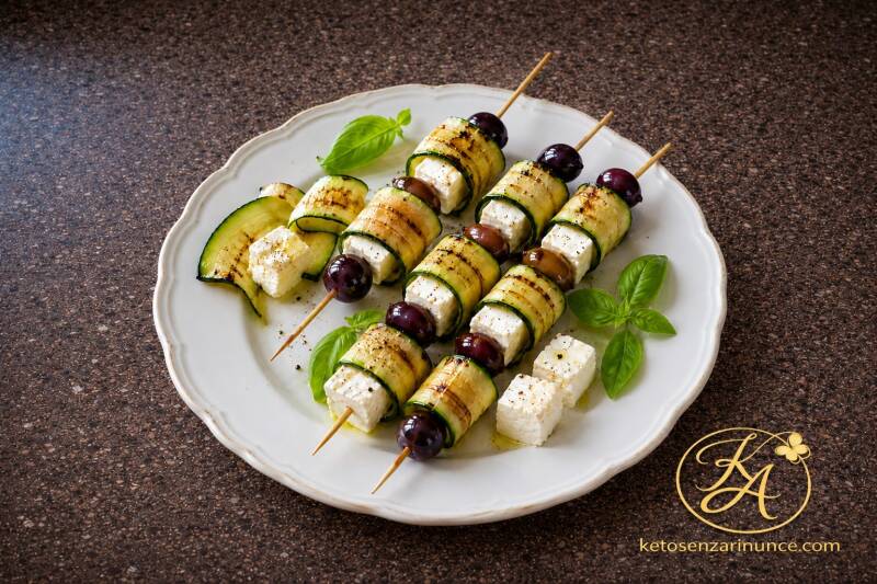 Spiedini keto di zucchine grigliate con feta e olive, una ricetta chetogenica estiva, semplice e mediterranea. Le zucchine grigliate avvolgono cubetti di feta e vengono alternate alle olive, con basilico fresco e olio extravergine d’oliva. 