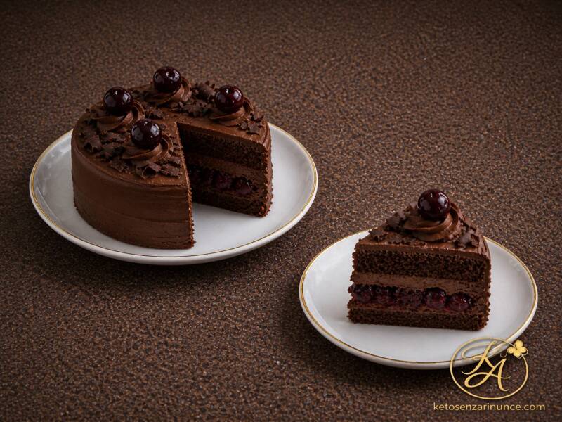 Torta piccola chetogenica al cioccolato con rum e amarena su piatto bianco con bordo oro, con fetta tagliata e ripieno di amarene