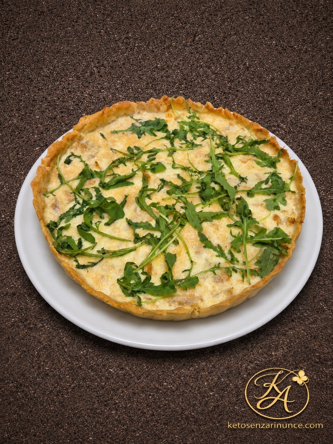 Torta salata keto con base di pasta brisée salata, ripieno cremoso con straccetti di pollo e scamorza, completata con rucola fresca. Una ricetta chetogenica estiva, golosa e adatta a un pasto completo con insalata fresca