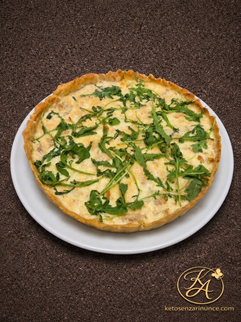 Torta salata keto con base di pasta brisée salata, ripieno cremoso con straccetti di pollo e scamorza, completata con rucola fresca. Una ricetta chetogenica estiva, golosa e adatta a un pasto completo con insalata fresca