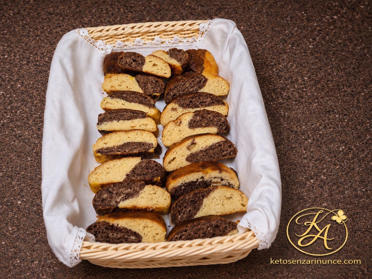 Treccina golosa per colazione keto bicolor, servita in un cestino su sfondo blog marrone con logo ketosenzarinunce.com. Una ricetta dolce chetogenica morbida alla vaniglia, cacao e noci, pensata per la colazione e da tagliare a fette.