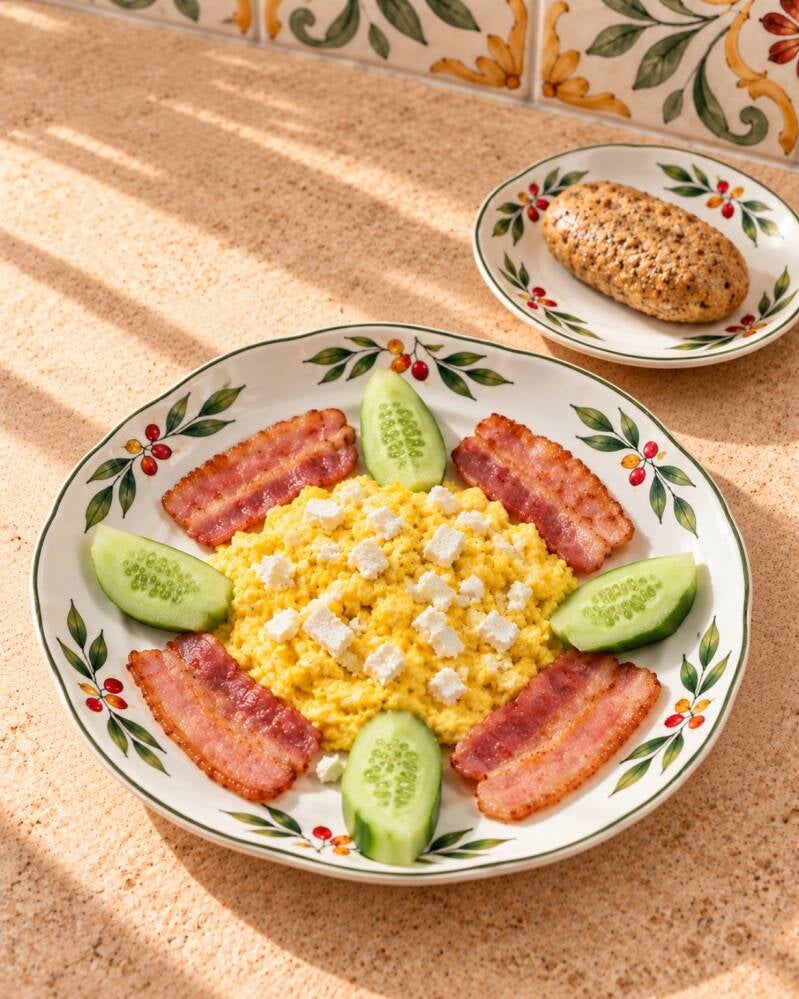 Colazione chetogenica salata con uova strapazzate cremose, bacon croccante, feta, cetriolo e pane keto ai semi. Un piatto completo, ricco e saziante, ideale per una colazione low carb.