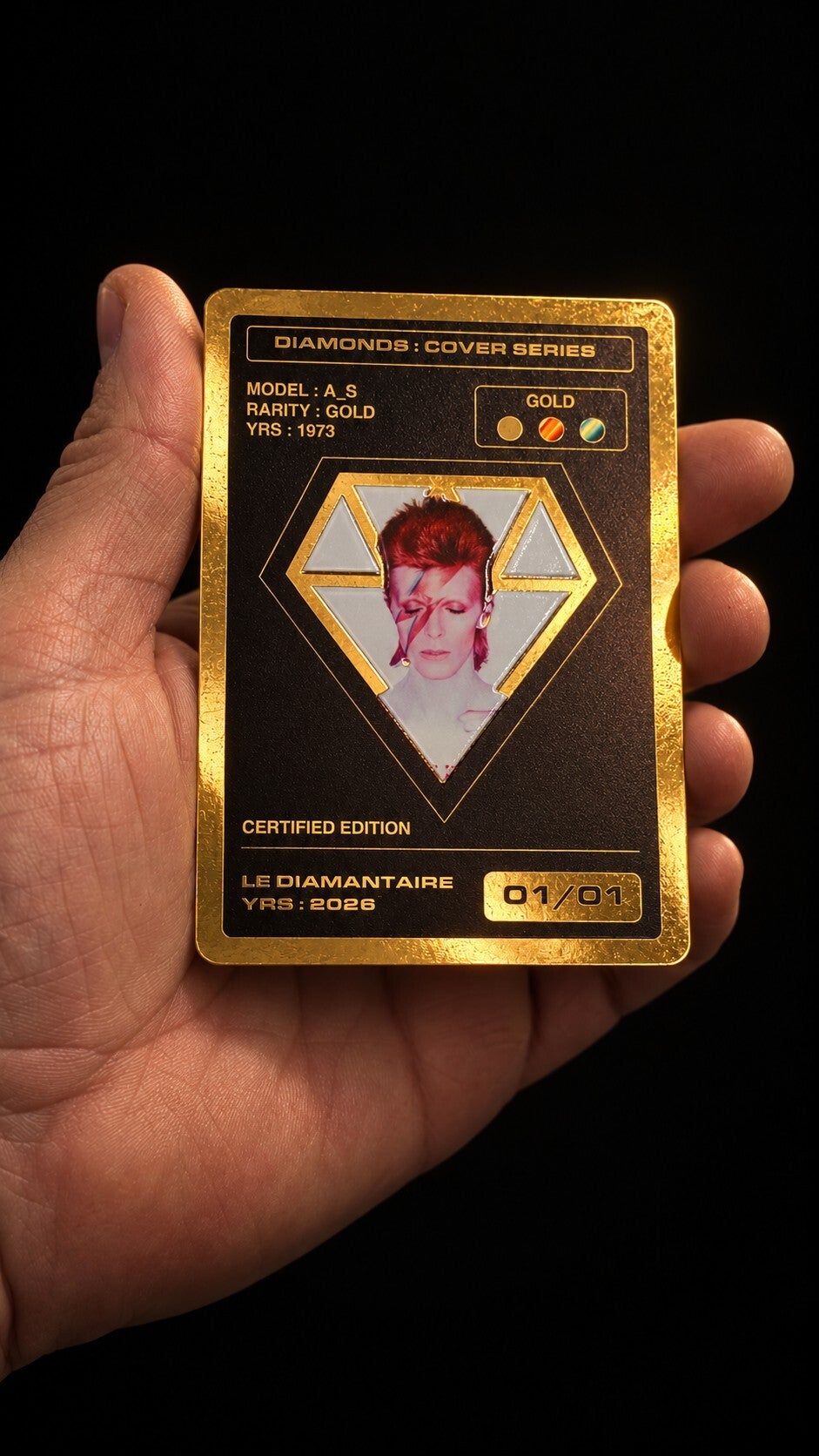 Une main tient la carte collector Gold Aladdin Sane, numérotée 01/01