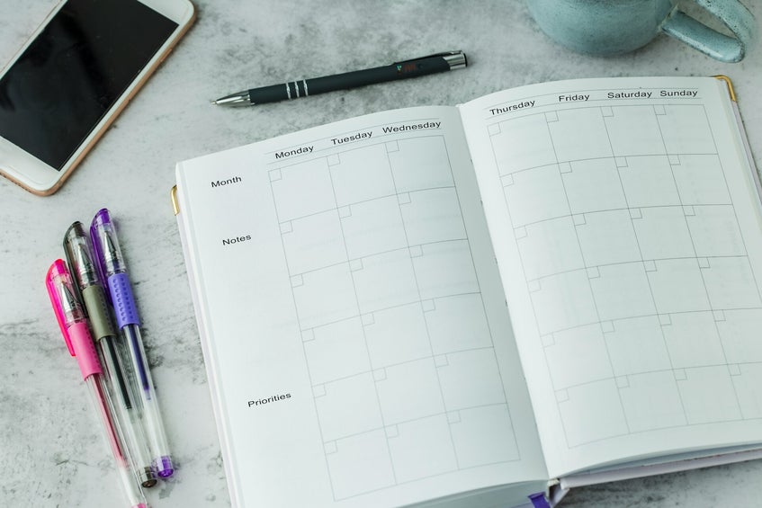 Open planner, pens, and smartphone white desktop