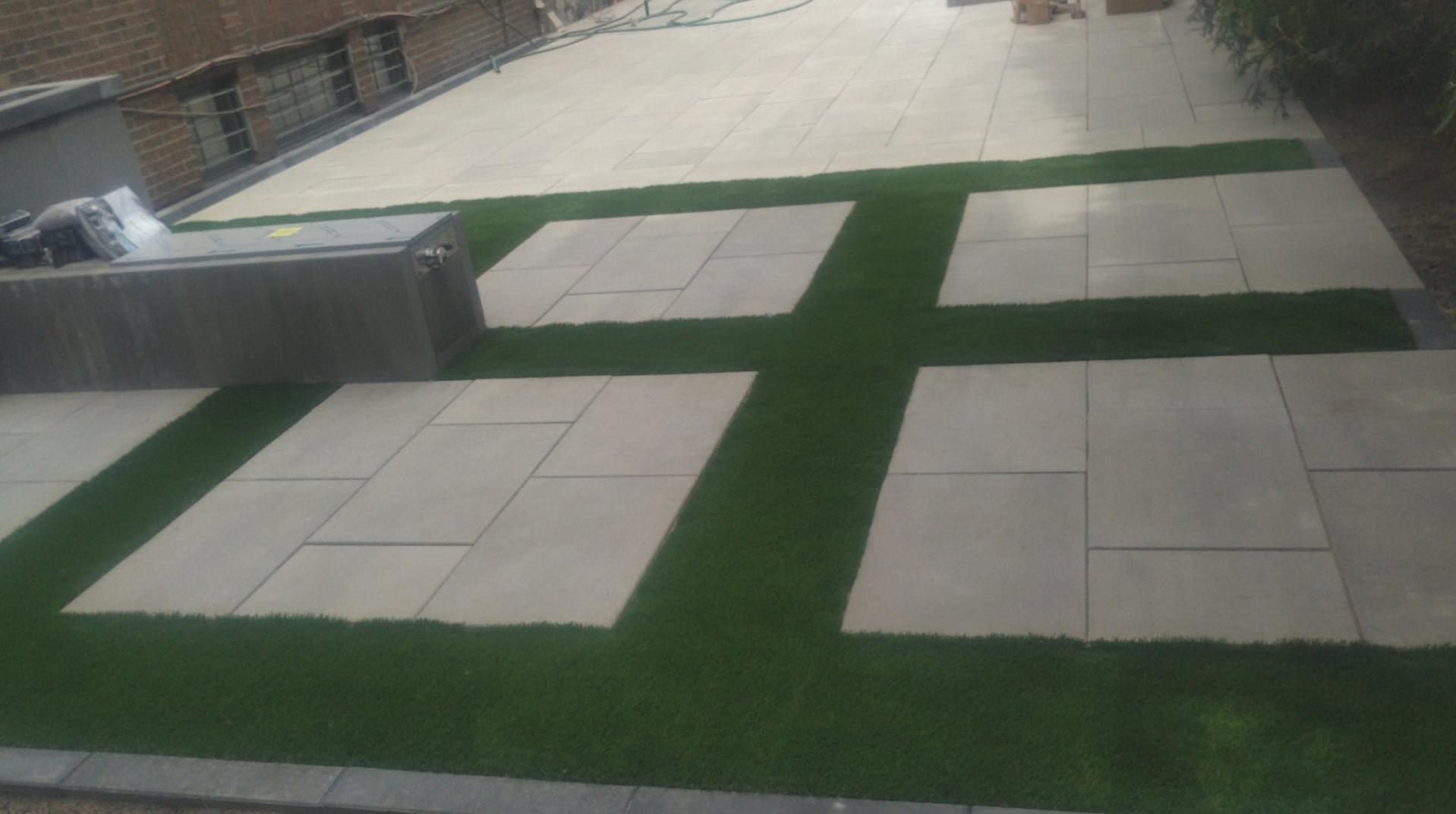 Gazon artificiel installé autour d’une surface en pavé uni à Montréal, espace extérieur entretenu