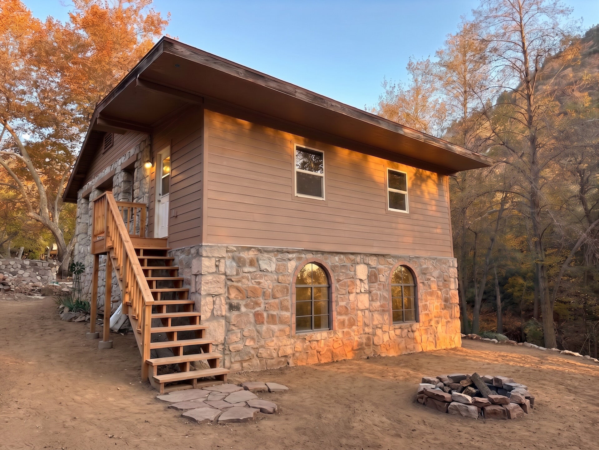 A cozy stone rental cabin in Ash Creek Canyon near Chrysotile, Arizona, with towering canyon cliffs in the background and a firepit in front of the cabin.