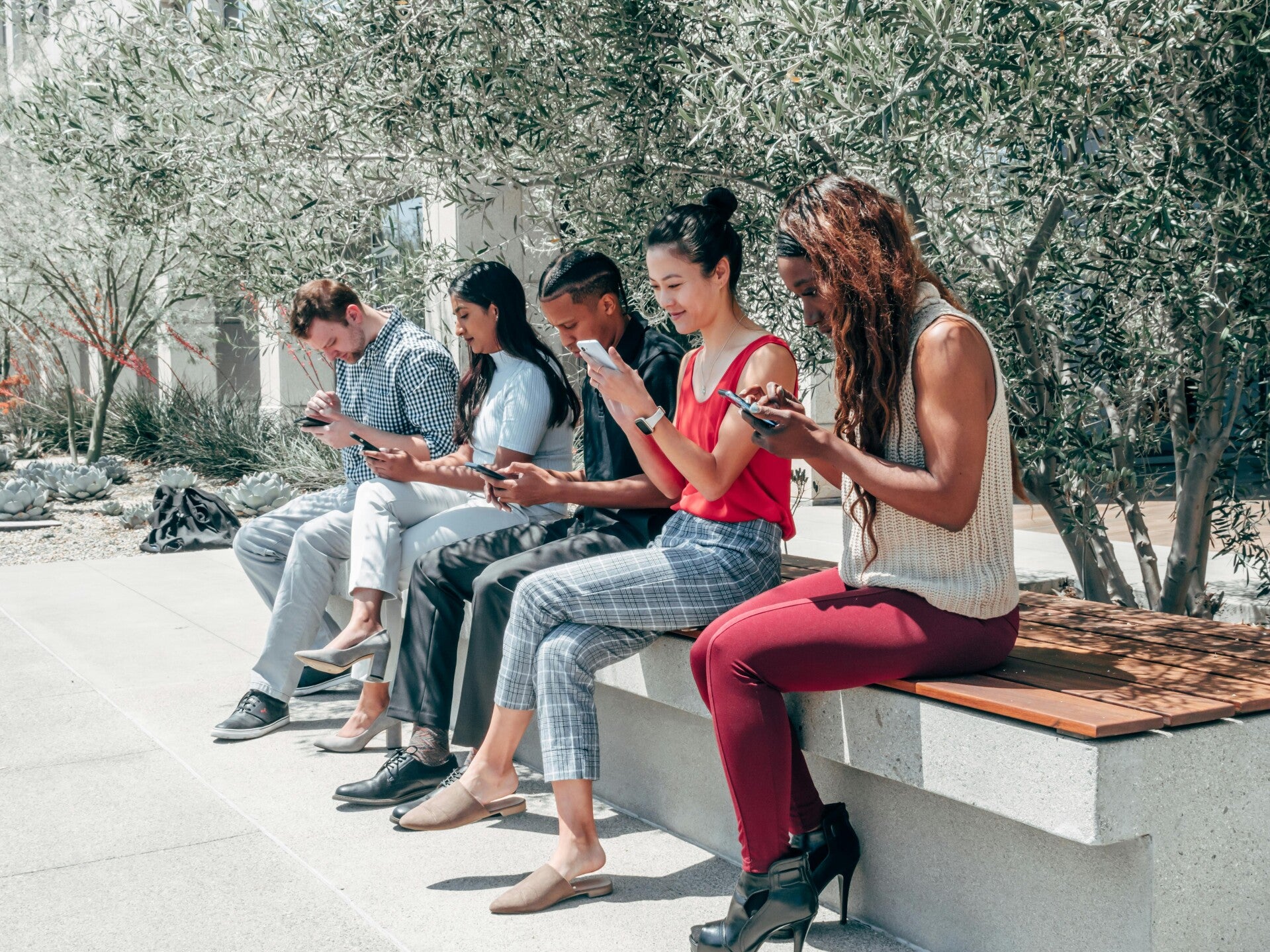 Five people in the sun on a bench, all engrossed in their own Social Media bubble on their phone.