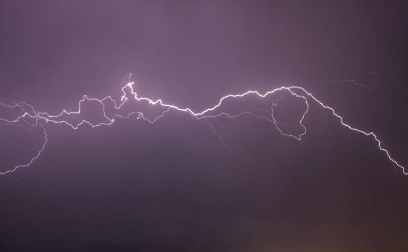 A jagged lightning bolt striking the ground, displaying a branching fractal pattern against a dark purple storm sky.
