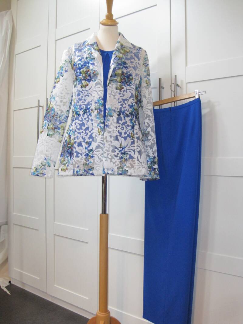 3-delig damespak met een blauwe rok en top, en een halftransparant wit jasje met blauwe bloemenprint. Maatwerk van Modestudio Jacoba.