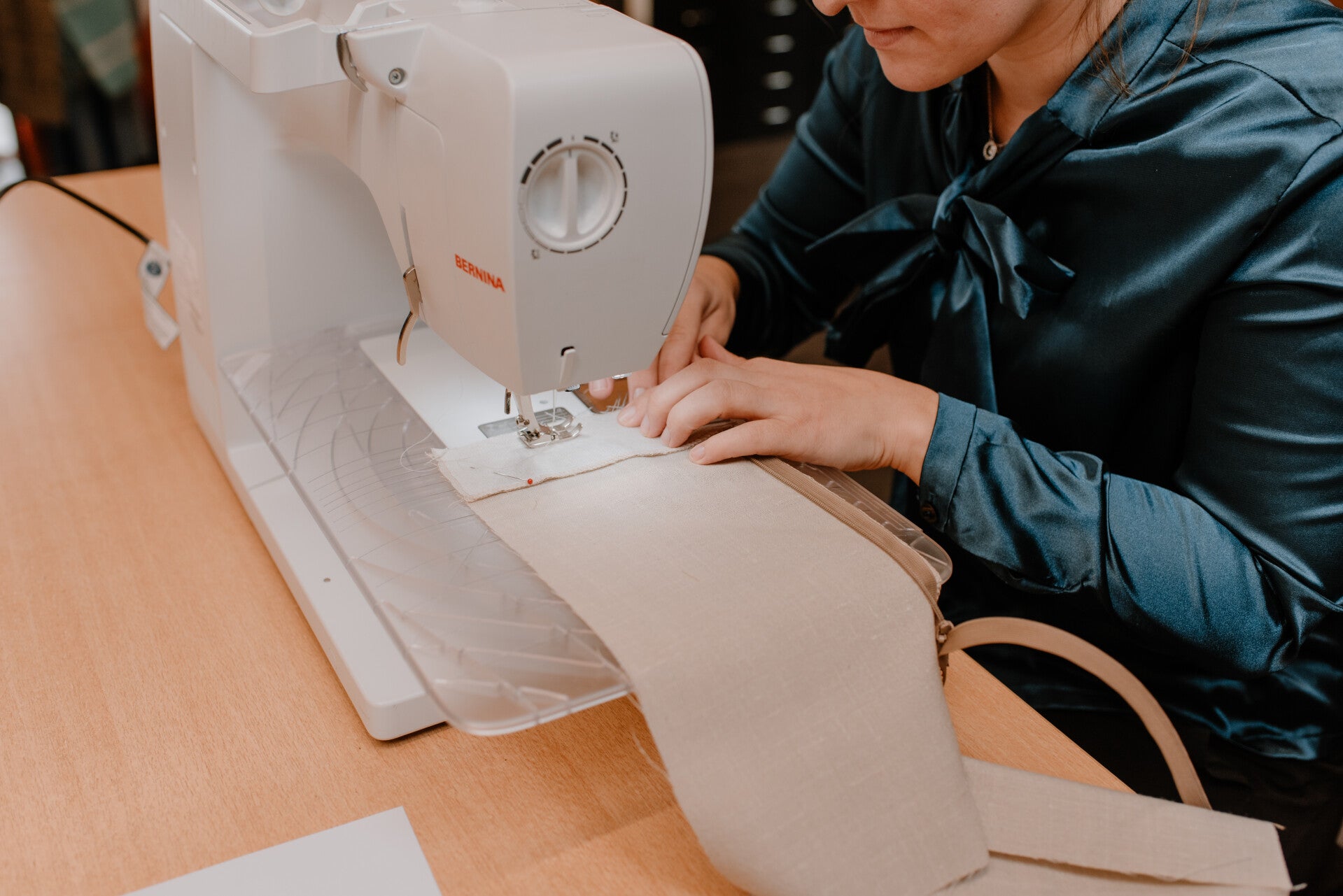 Sfeerimpressie van de opleiding tot costumière. Een cursist zit achter de naaimachine en is aan naaien, ze draagt een donkergroene blouse.