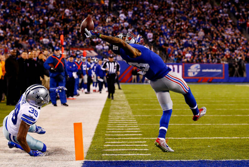 un joueur de foot américain (Odell Beckham Jr) en pleine réception de la balle sur un terrain de foot en plein match