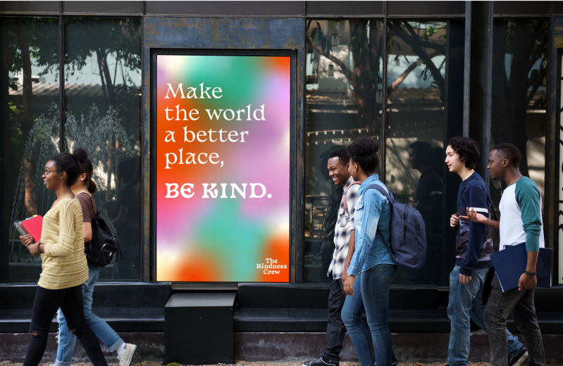 Een groep studenten loopt langs een grote poster, waarop staat: Make the world a better place, be kind.