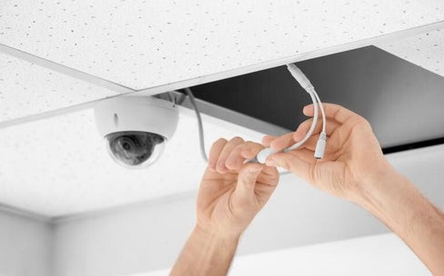 Un technicien en système de sécurité procède au branchement d'une caméra de vidéosurveillance.