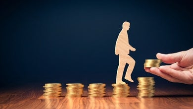 Un homme monte sur des pièces de monnaie sur une table en bois, représentant la progression financière.