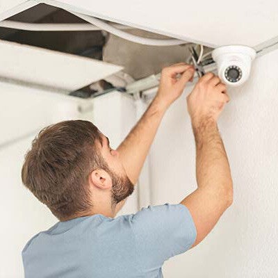 Un homme en train d'installer une caméra de sécurité sur un mur.
