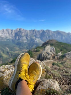 Persona descansando con zapatillas amarillas en primer plano, sentada entre rocas y con vista a la cordillera de los Picos de Europa.