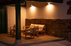 Vista nocturna del exterior de Armaño 12 con porche cubierto, bancos de madera y zona ajardinada con iluminación decorativa.