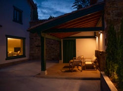 Zona de porche iluminado por la noche con sillones de madera y cojines claros, ideal para relajarse en Armaño 12.