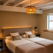 Dormitorio acogedor con dos camas individuales, cabecero tapizado en tono beige, lámpara colgante de mimbre y luz ambiental cálida, en la casa rural Armaño 12