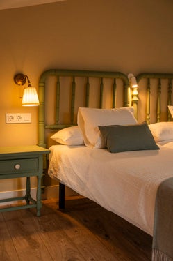 Habitación con cama doble, cabecero clásico de madera verde, mesita a juego y luz cálida de lectura, en la casa rural Armaño 12.