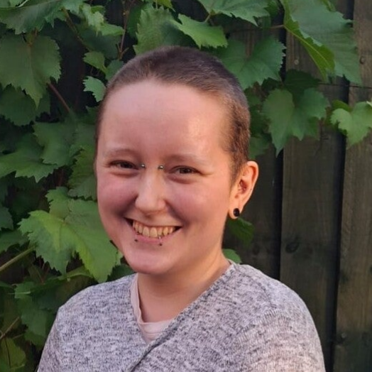smiling young person looking at camera with piercings, on a natural green backdrop