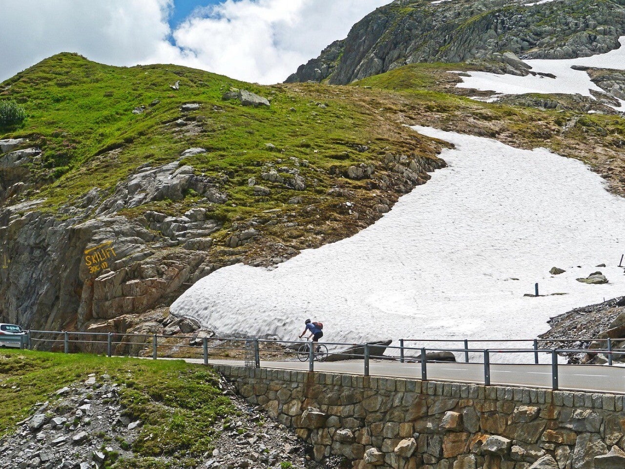 Road cyclist riding beside summer snow on Switzerland’s Susten Pass