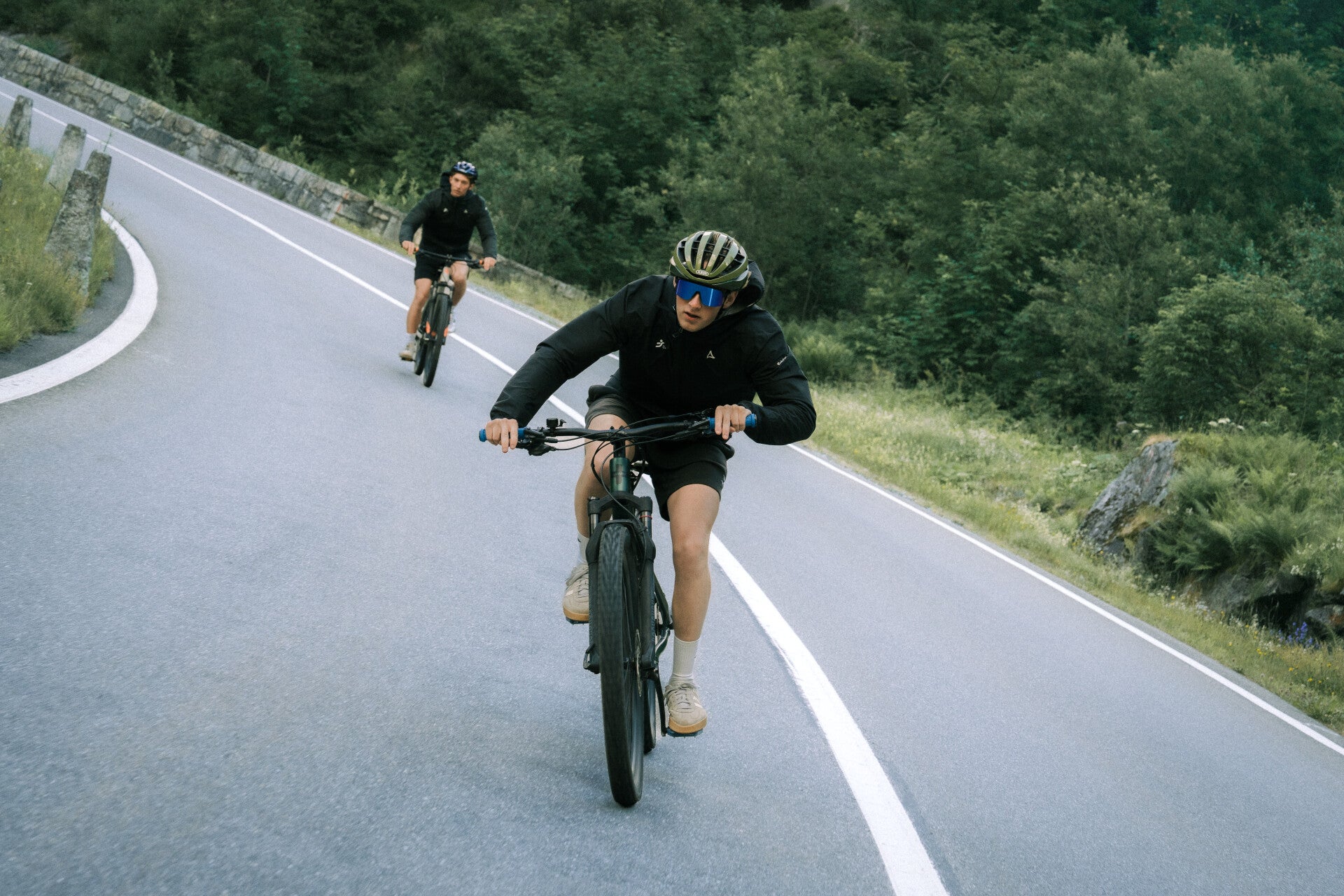 Two cyclists climbing a winding Swiss mountain road
