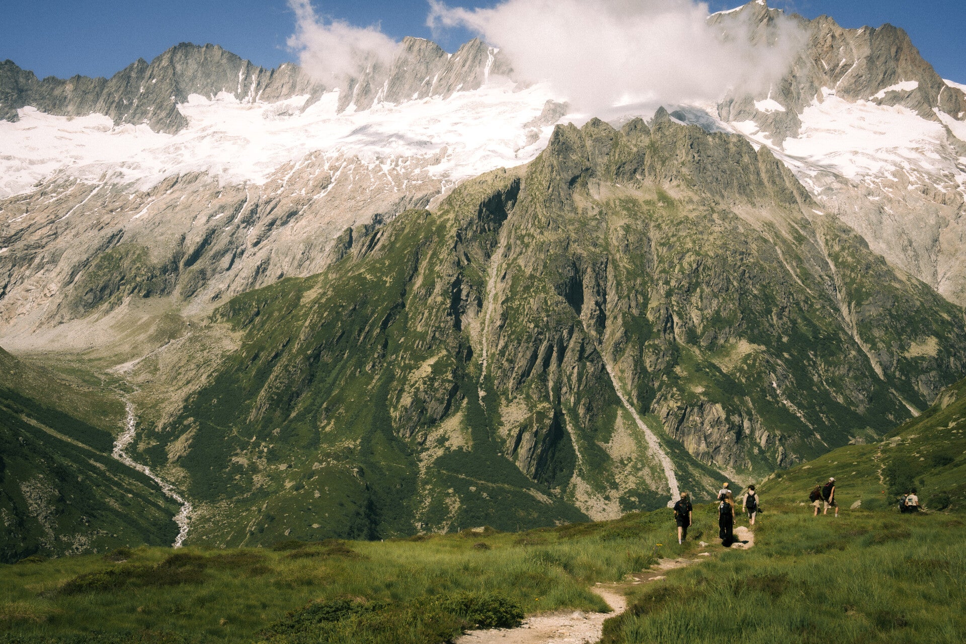 Hikers crossing a high Swiss Alpine landscape beneath glacier peaks