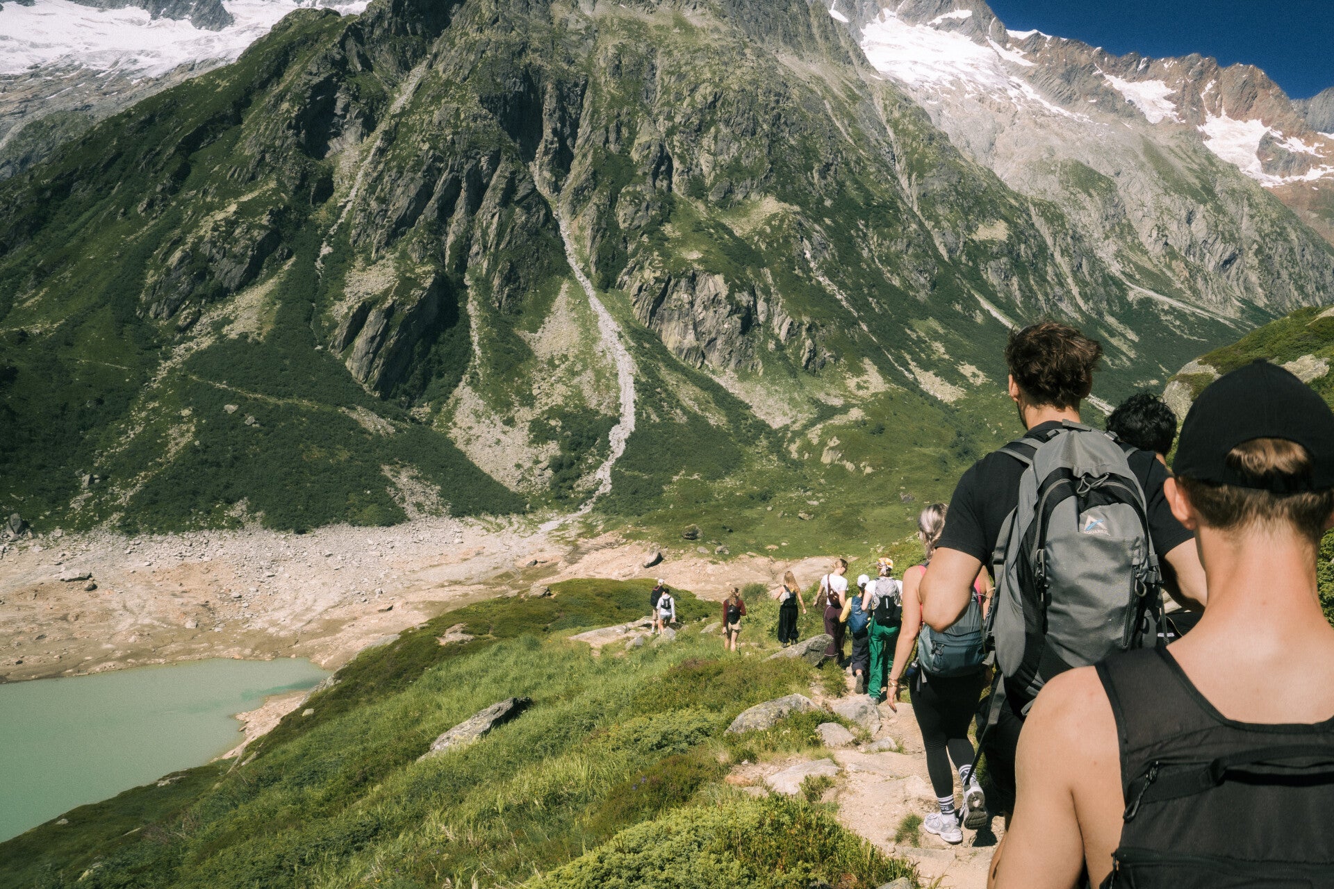 Guided hiking group descending an Alpine trail beneath high peaks
