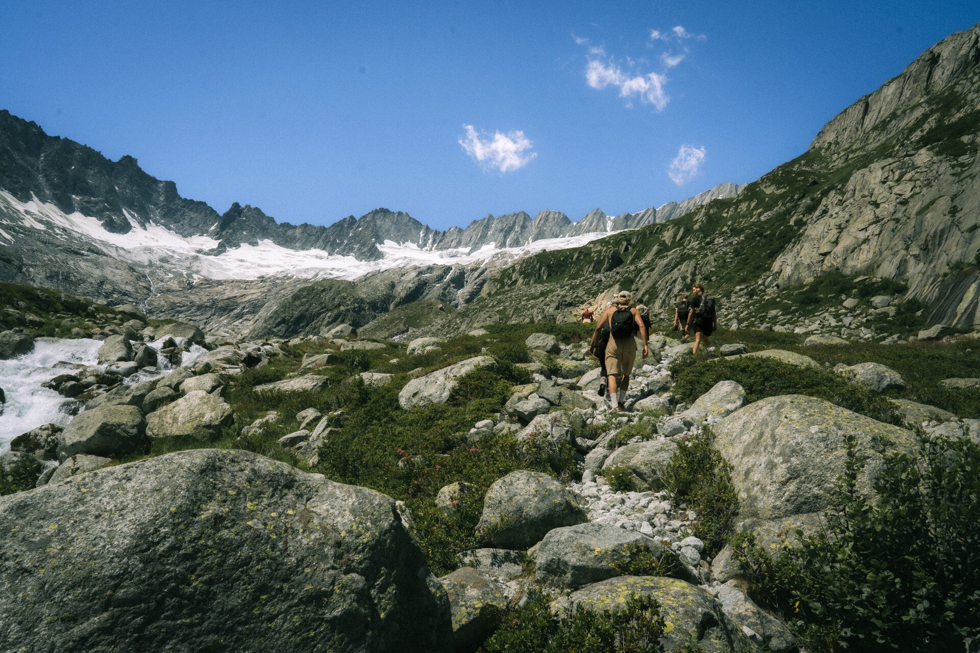 Hikers following a rocky trail beneath Swiss Alpine glacier peaks