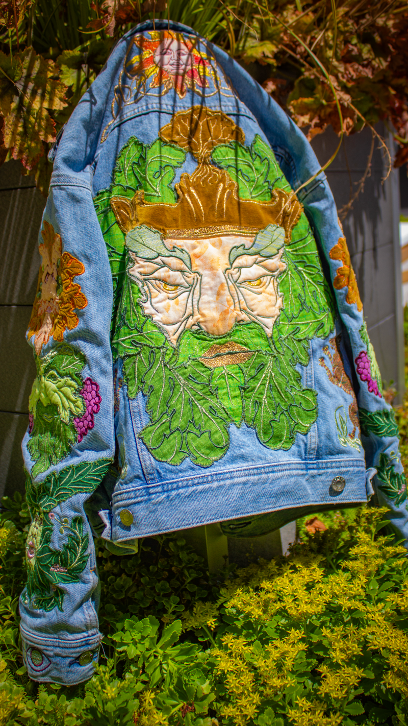Back of a denim jacket with a large colorful tattoo-inspired greenman embroidery filling most of the back panel.