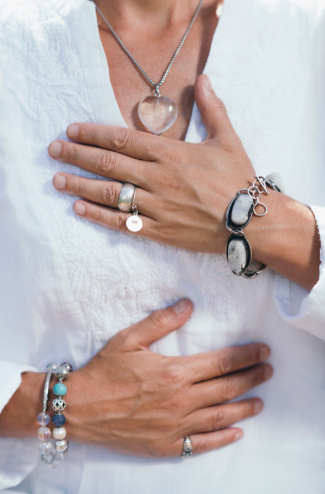 Foto van een spirituele vrouw met een bergkristallen hanger en haar handen op haar borst en buik.