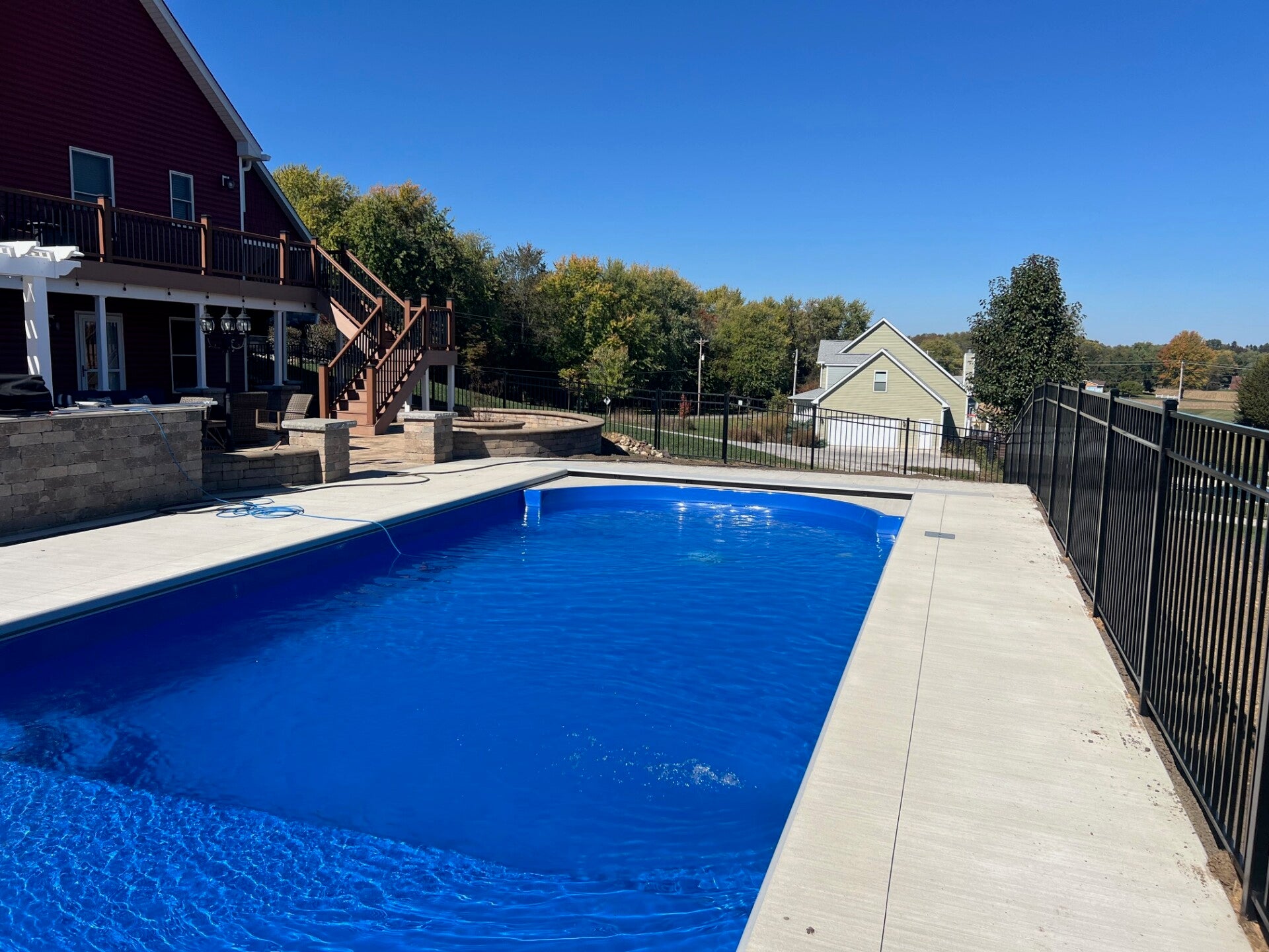 A backyard pool framed by the house, deck, and fence.
