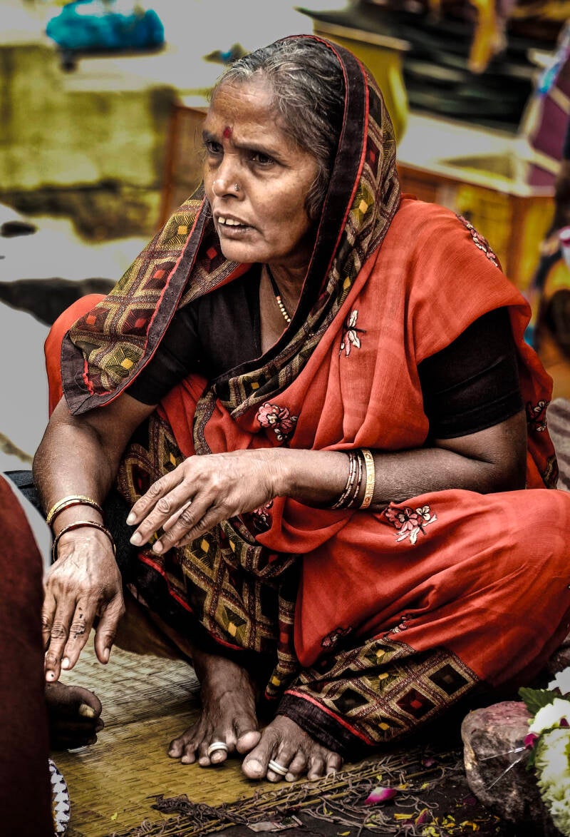 Street photography Varanasi, India: colourful, beringed lady focussed on prayers speak