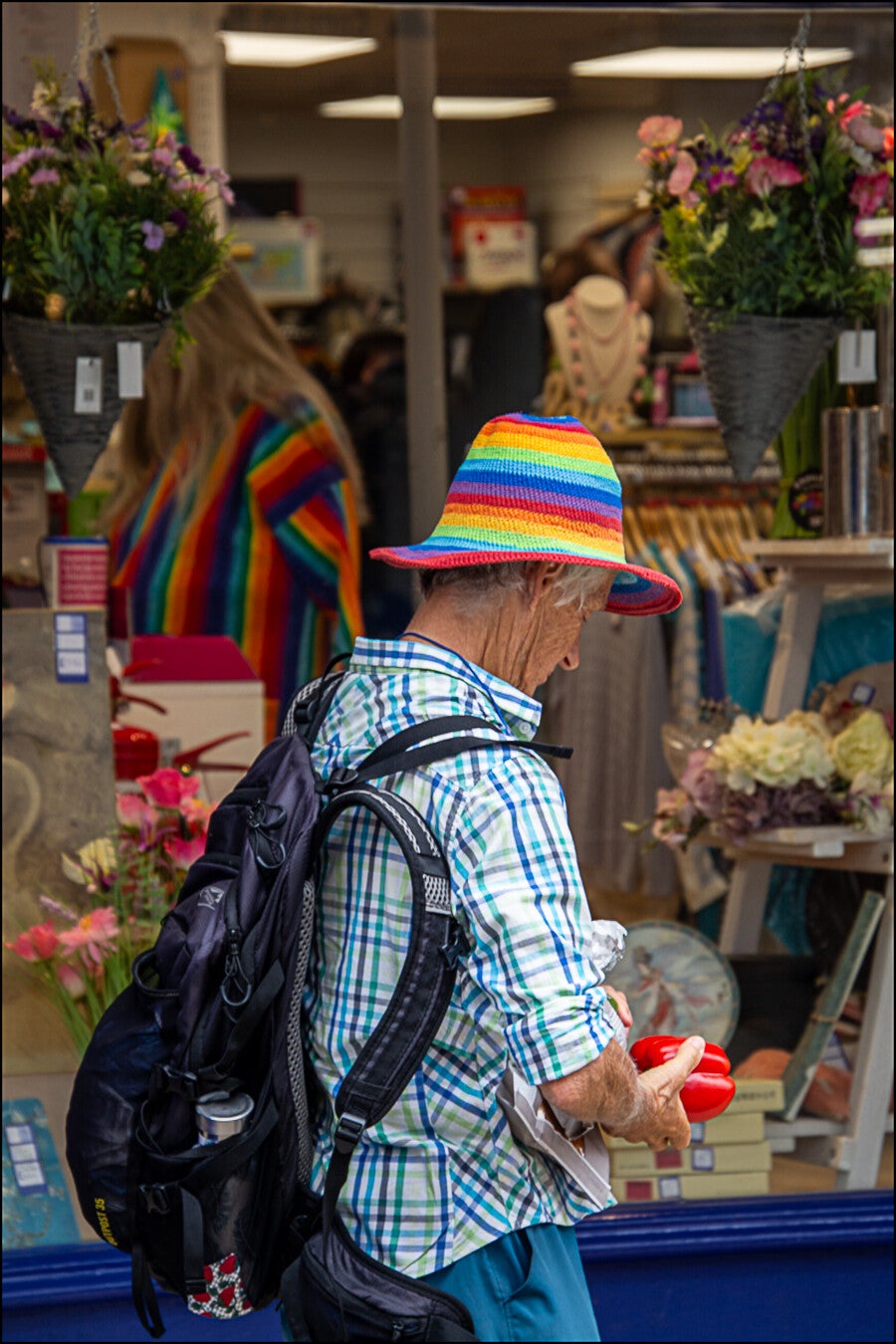 Street photography of a man wearing a colourful striped hat passing a shop window, photographed by Robbie Clymo.