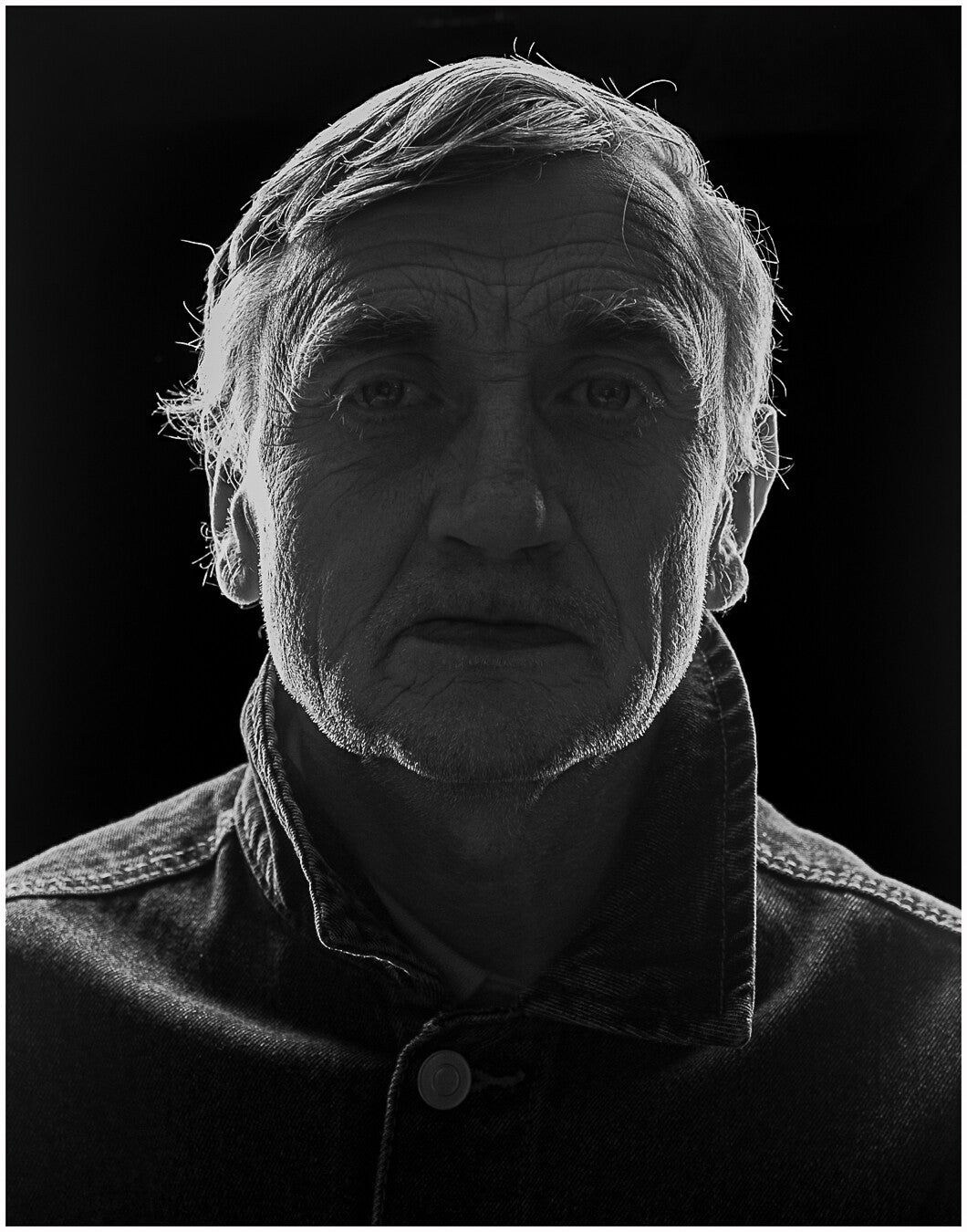 Black and white portrait of Paul facing the camera, dramatically backlit against a dark background.