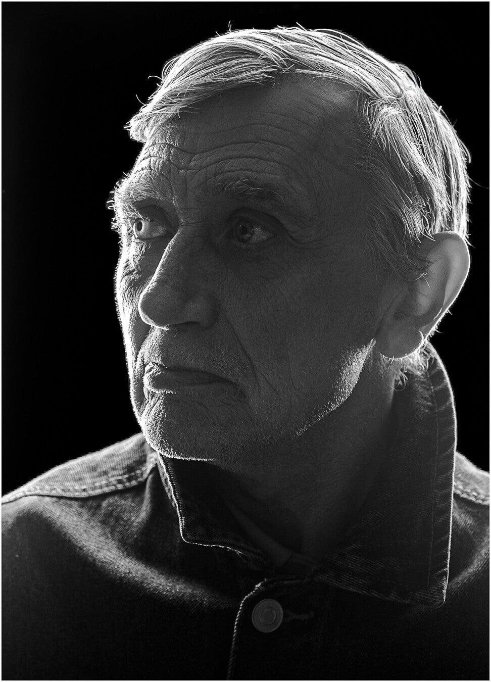 Black and white portrait of Paul facing the camera, dramatically backlit against a dark background