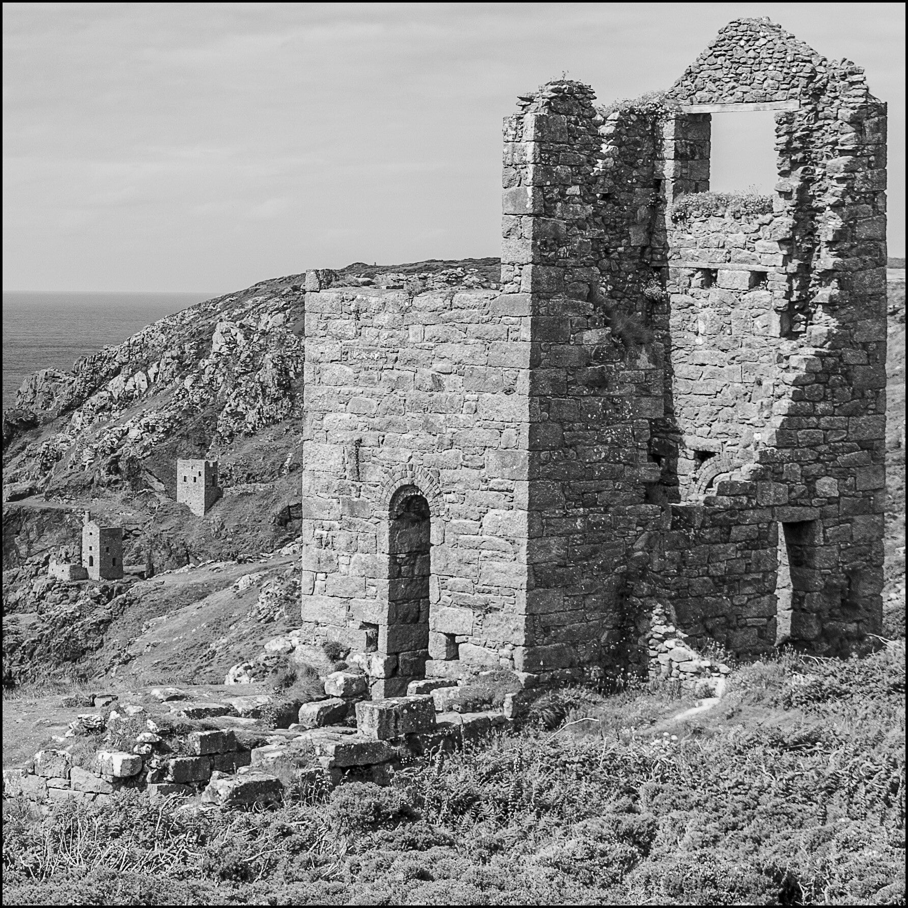 Black and white photograph of historic Cornish mine workings and ruined engine houses on the coast.