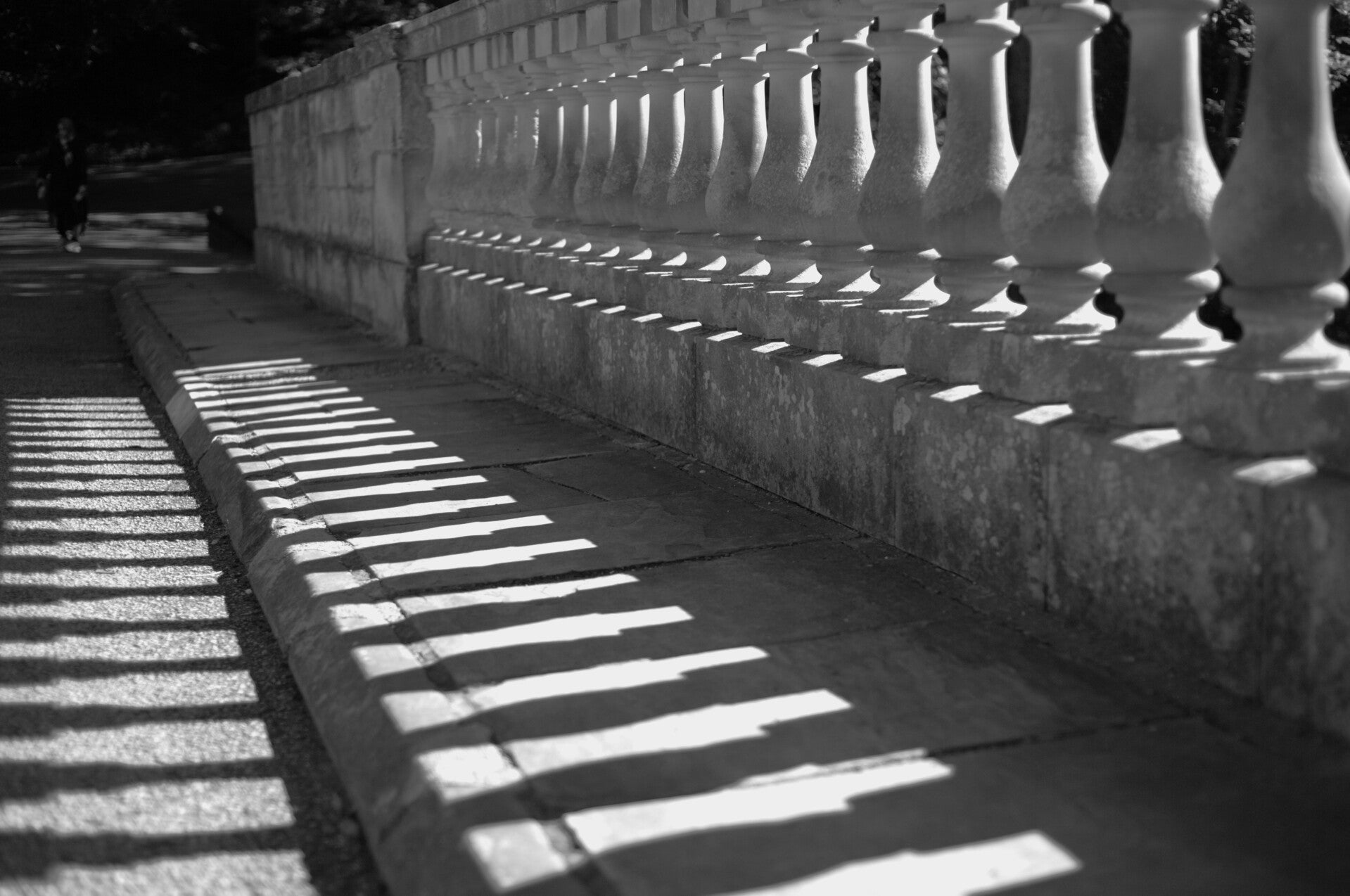 Black and white photograph of sunlight casting repeating shadows through a stone balustrade.