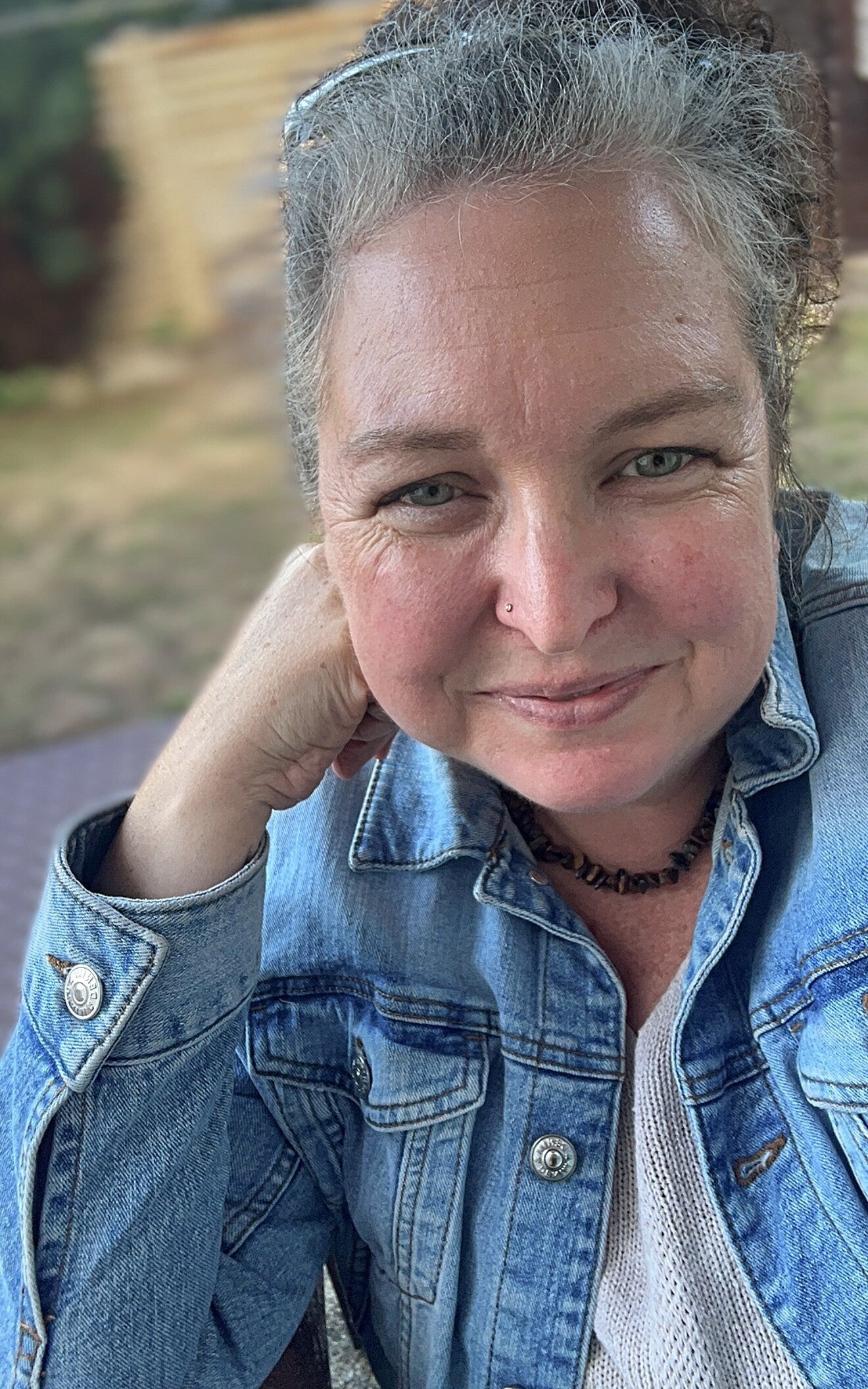 Die Frau auf dem Foto trägt eine blaue Jeansjacke, hat mittellanges, dunkles Haar und blickt mit einem freundlichen Ausdruck direkt in die Kamera.