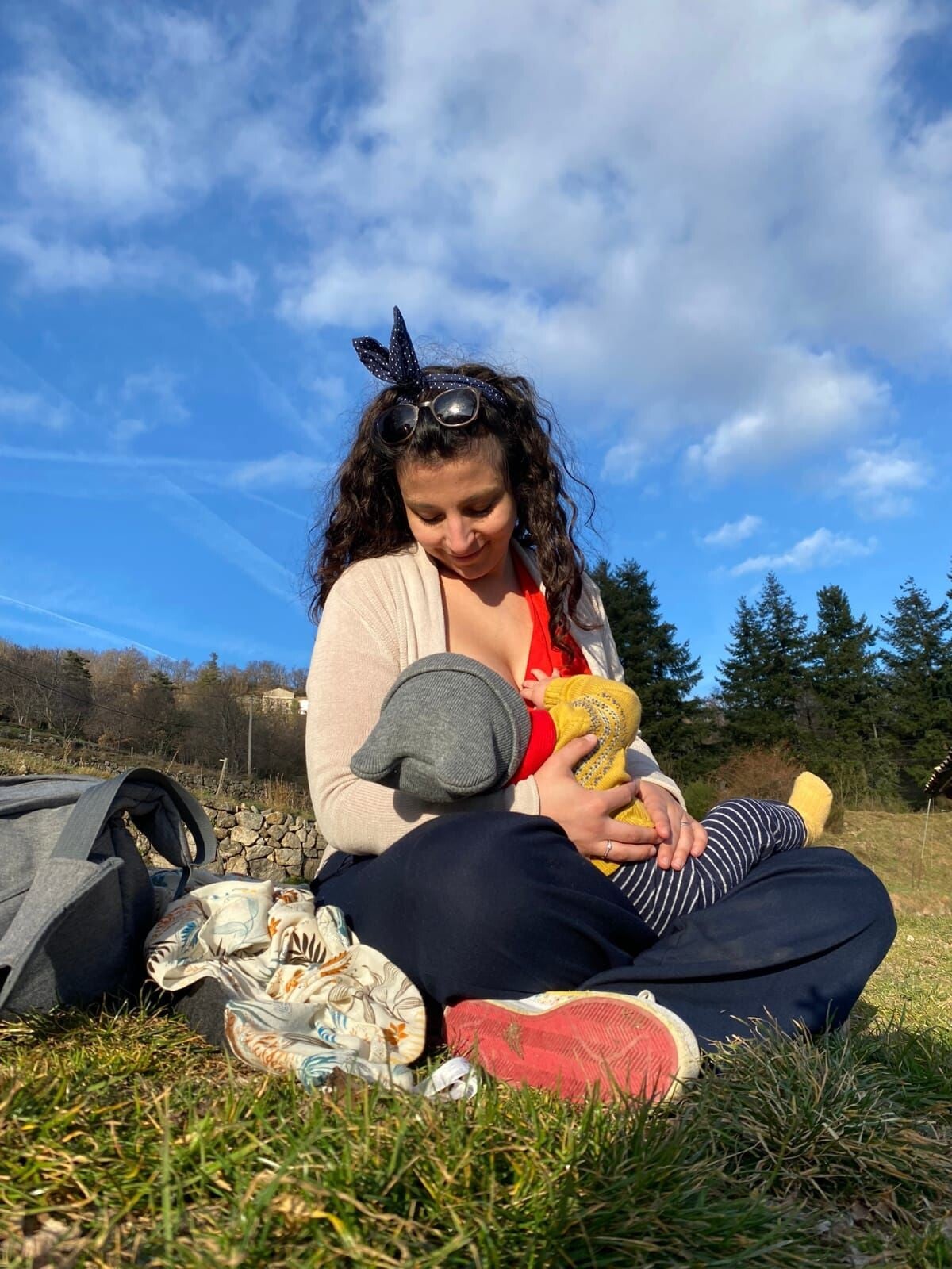 Femme allaitante. maman qui allaite dans la nature bébé . posée dans l'herbe . sapin. ciel bleu