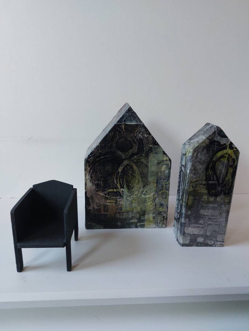 Dijkhuisje Ik mis je 2, 2023 in elk huis is een lege stoel waar iemand wordt gemist. Houten huisje met mixed media met collage zelfbedrukt papier met houten ministoeltje