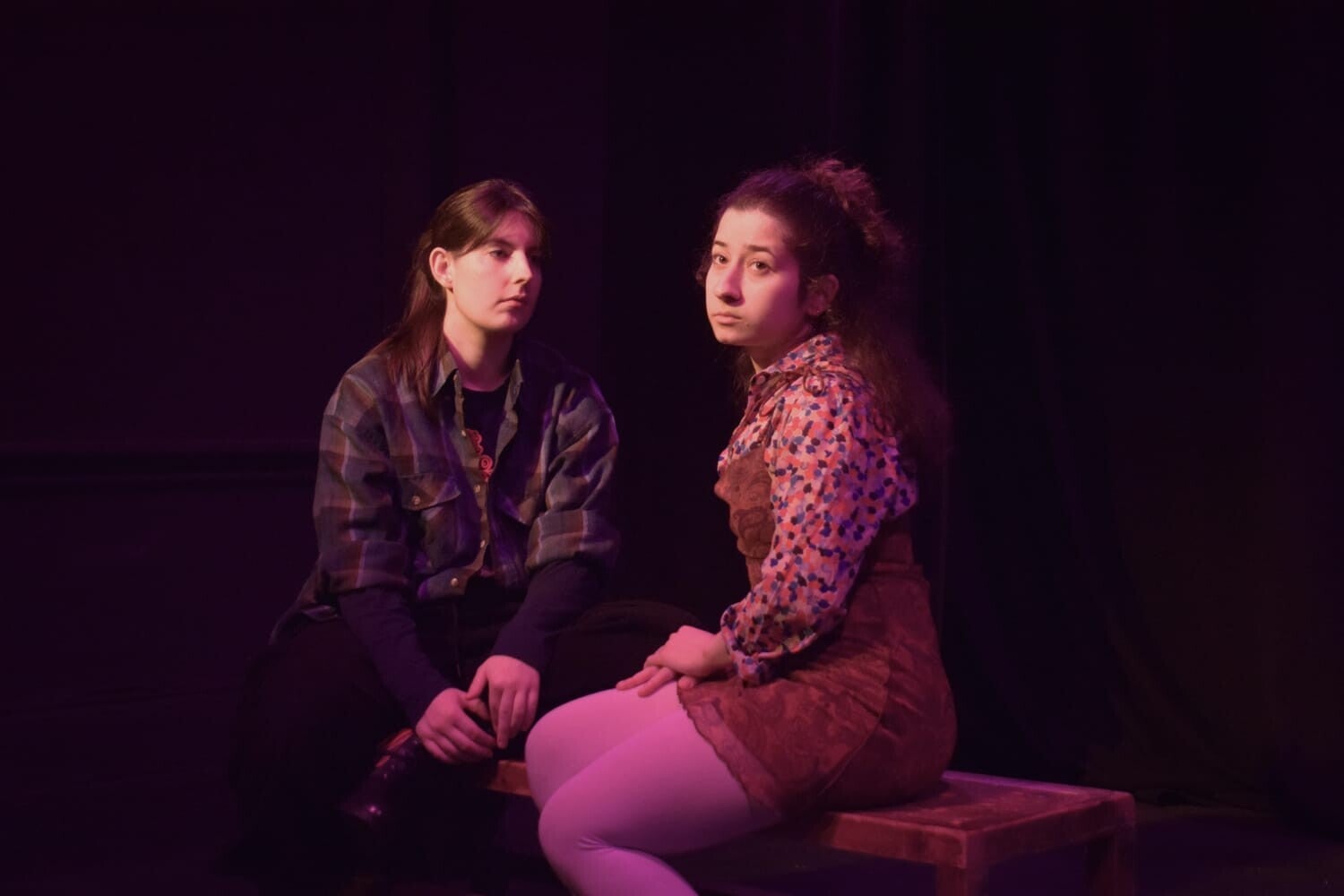 Two people huging while someone watches them while sitting on a sofa. They are on stage.