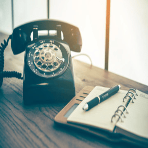 Auf einem Holztisch liegen ein Vintage-Telefon, ein Notizbuch und ein Stift, im Kontext mit Jenseitskontakte Jana Lorenz.