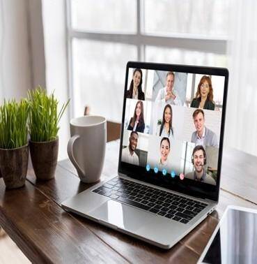 Laptop auf Holztisch zeigt neun Personen in einem Videoanruf, daneben zwei Pflanzen in Töpfen und eine weiße Kaffeetasse, im Kontext der Großen Gruppenlesung mit Medium Jana Lorenz.