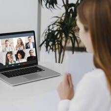  Eine Frau sitzt an einem Tisch mit einem Laptop, auf dem eine Videokonferenz mit mehreren Personen angezeigt wird, im Kontext mit Jenseitskontakte Jana Lorenz.